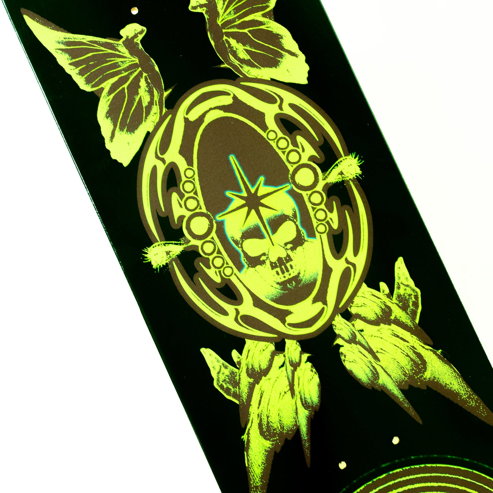 A close-up of a skateboard deck featuring a black background with a glowing neon yellow-green graphic of a skull inside an ornate oval frame, surrounded by butterfly wings and floral elements.